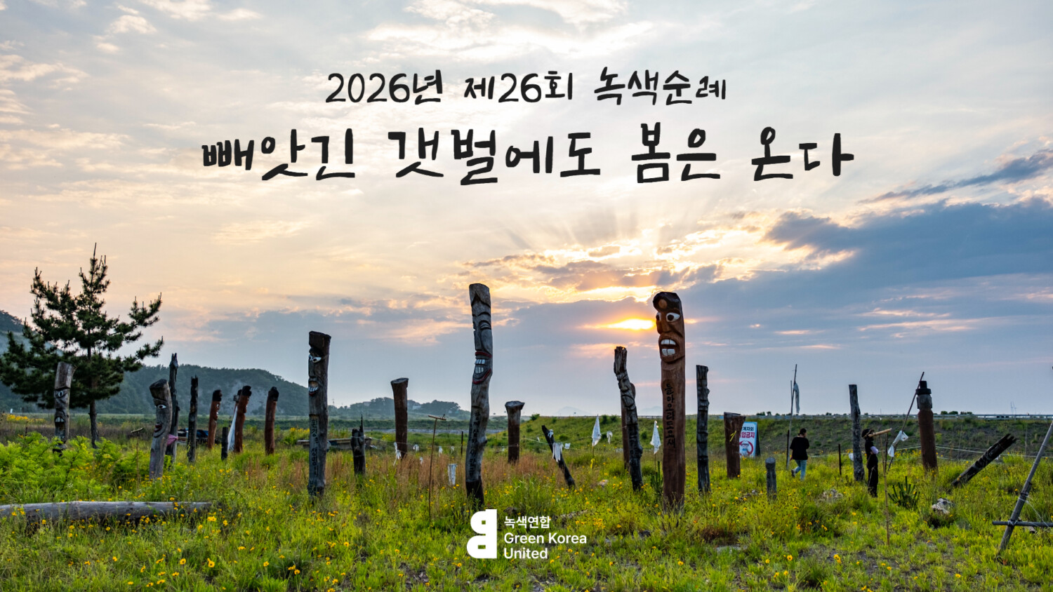 2026년 제26회 녹색순례 빼앗긴 갯벌에도 봄은 온다 메인 이미지. 새만금 개발 사업으로 육지가 되어버린 해창갯벌에 장승 수 십 개가 세워져 있다. 뒤로는 구름 사이로 해가 보인다.